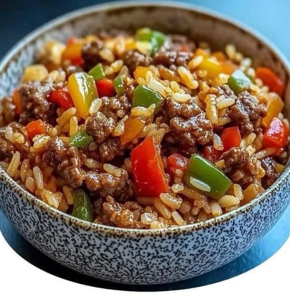 A bowl of beef and pepper stir-fry served over fluffy white rice, garnished with sesame seeds