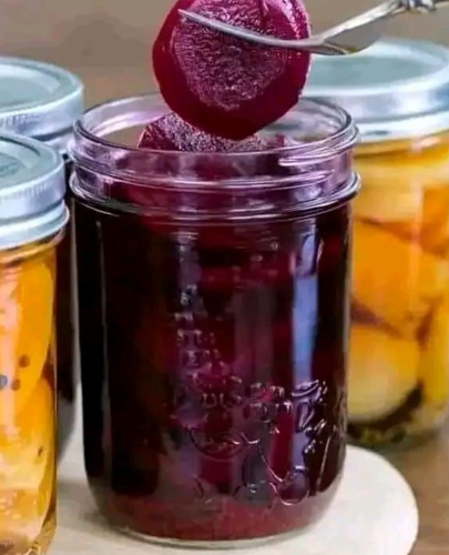 A jar of homemade pickled beets with vibrant purple color, garnished with cloves and allspice, ready to be served.