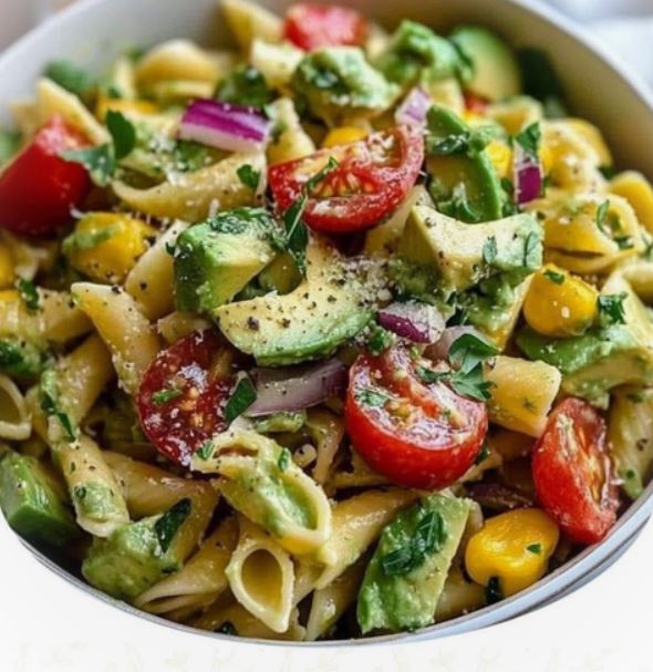 A vibrant avocado pasta salad with cherry tomatoes, cucumbers, and feta, served in a white bowl