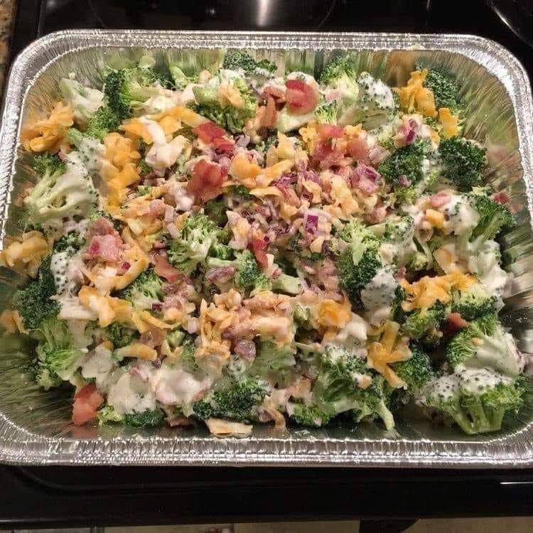A colorful bowl of creamy broccoli salad with cheddar cheese, crispy bacon, and red onions, served cold