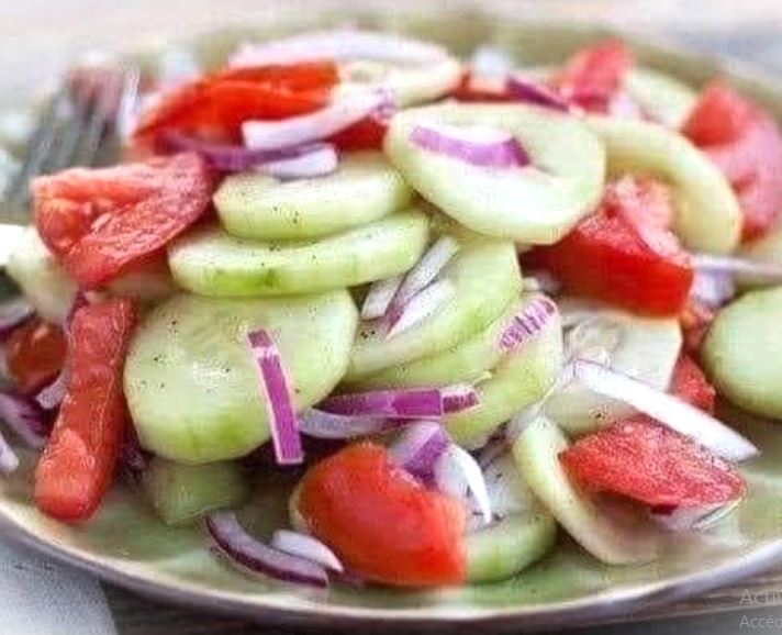 A bowl of fresh marinated cucumber, onion, and tomato salad with a tangy lime dressing