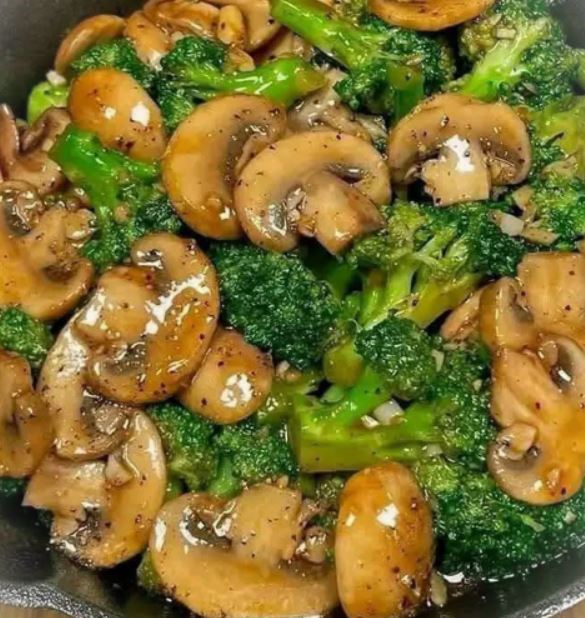 A plate of vibrant stir-fried mushrooms and broccoli, garnished with sesame seeds and green onions