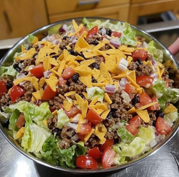 A large bowl of Dorito Taco Salad made with seasoned ground beef, shredded lettuce, tomatoes, red onions, cheddar cheese, and crushed nacho chips
